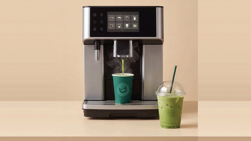 Coffee machine dispensing a matcha latte into an Allreasons cup, iced matcha to-go cup beside it