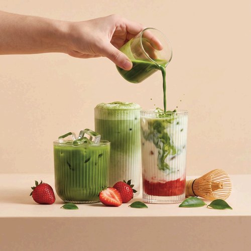 Matcha poured over two iced matcha lattes with strawberries and a whisk